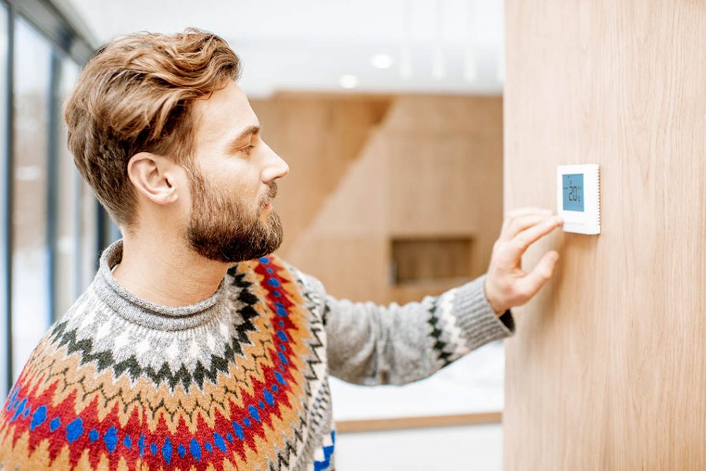 Man in sweater adjusts thermostat